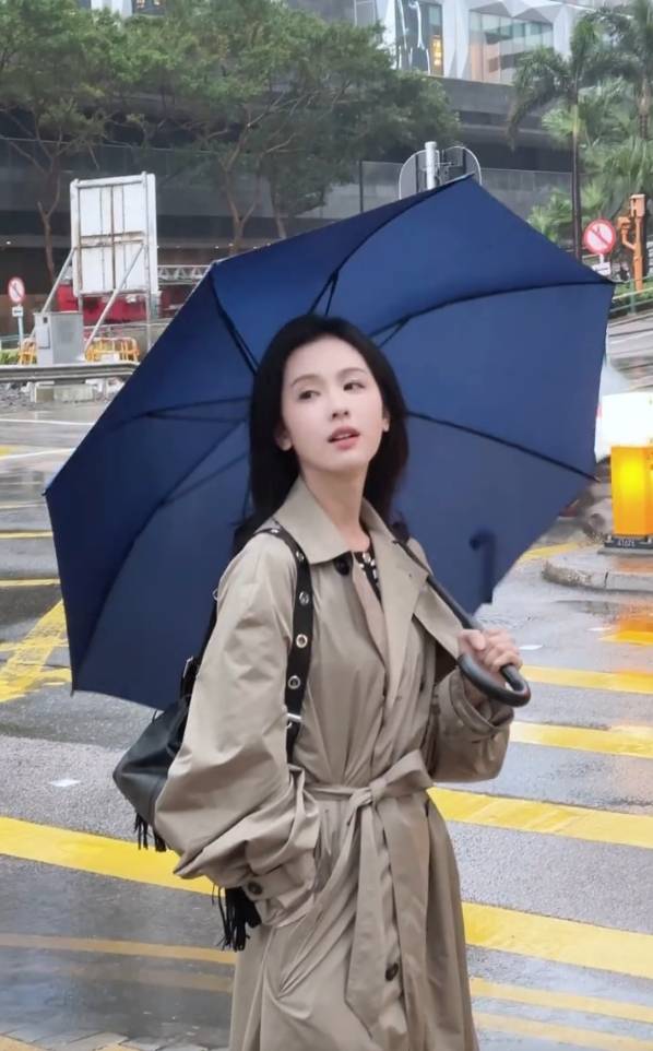 陈都灵着驼色风衣手持蓝伞 雨中街头随拍眼神清澈