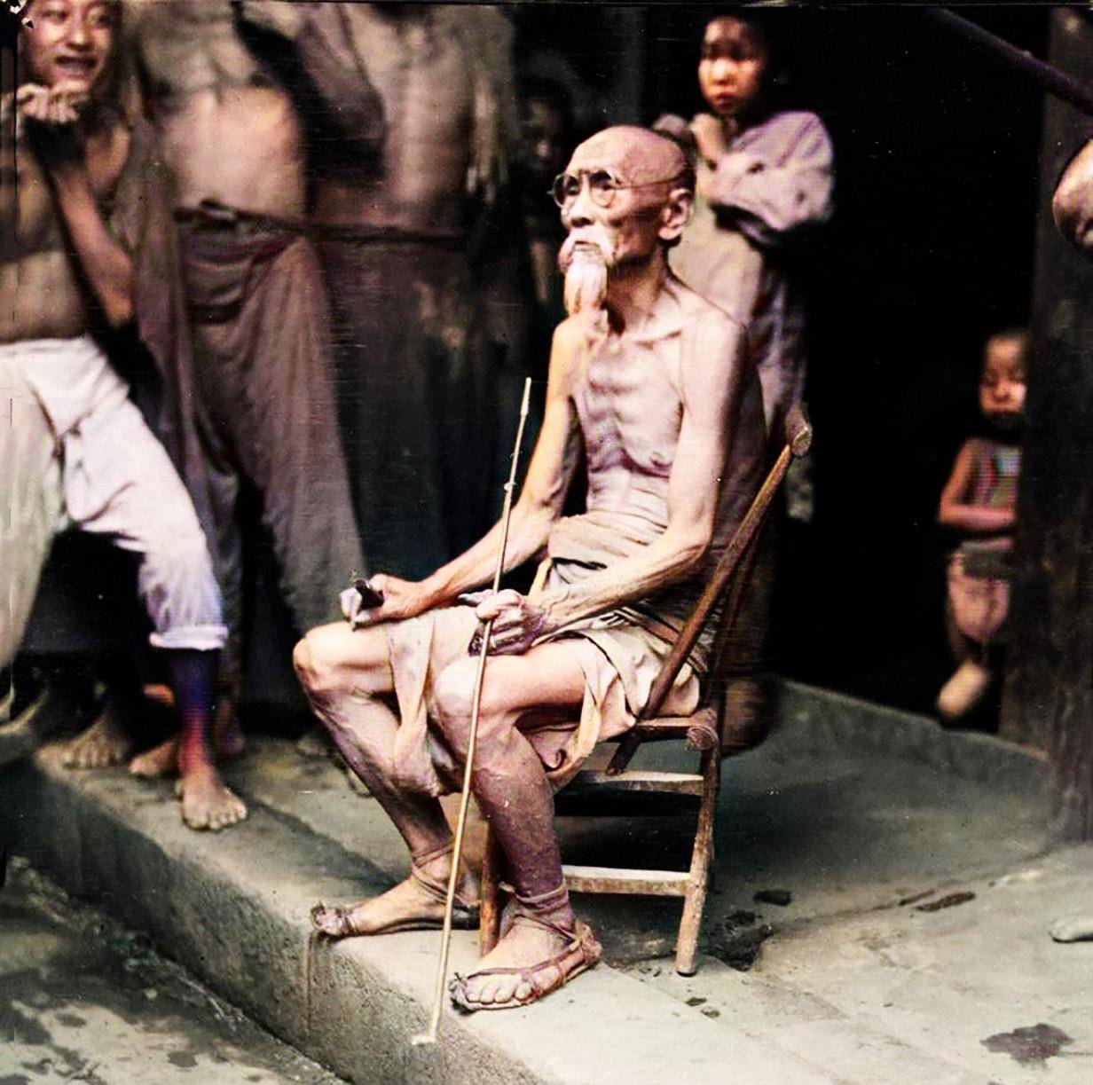 抽烟的老者一位白胡子老人坐在街边的竹椅上,手里拿着一根长长的烟杆.