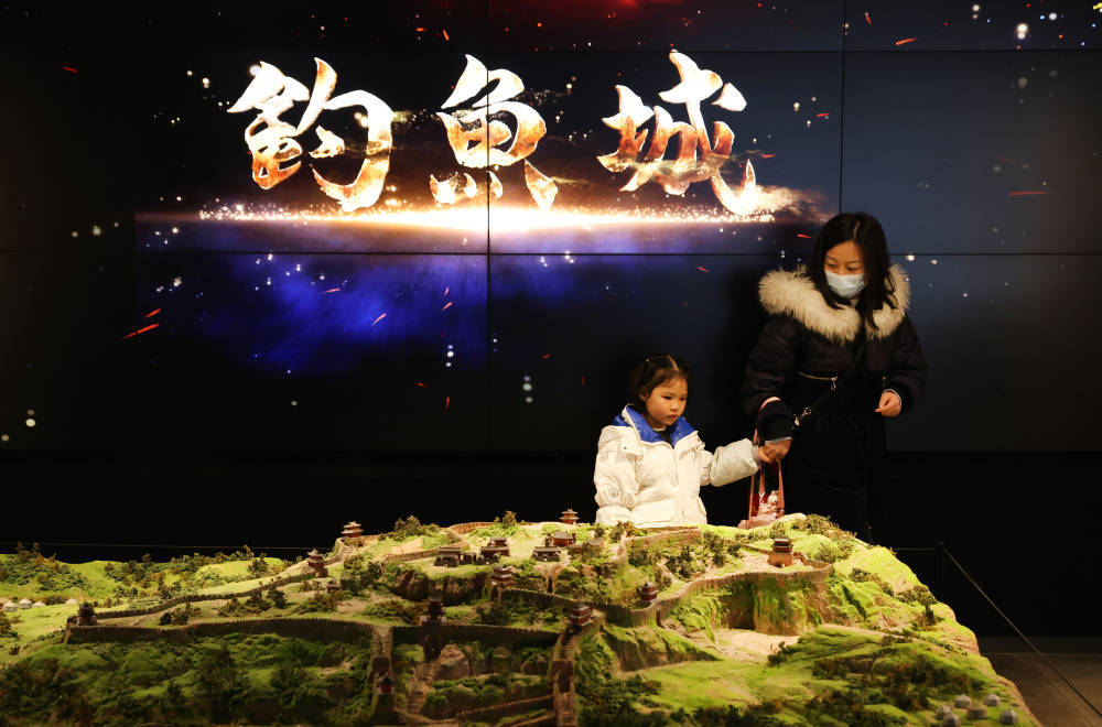 一家长正带着孩子参观钓鱼城模型.