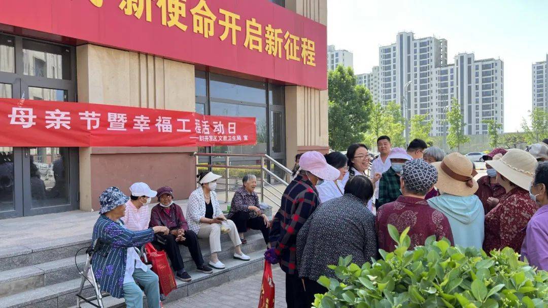 活动现场悬挂"母亲节暨幸福工程活动日"条幅,工作人员向过往居民发放