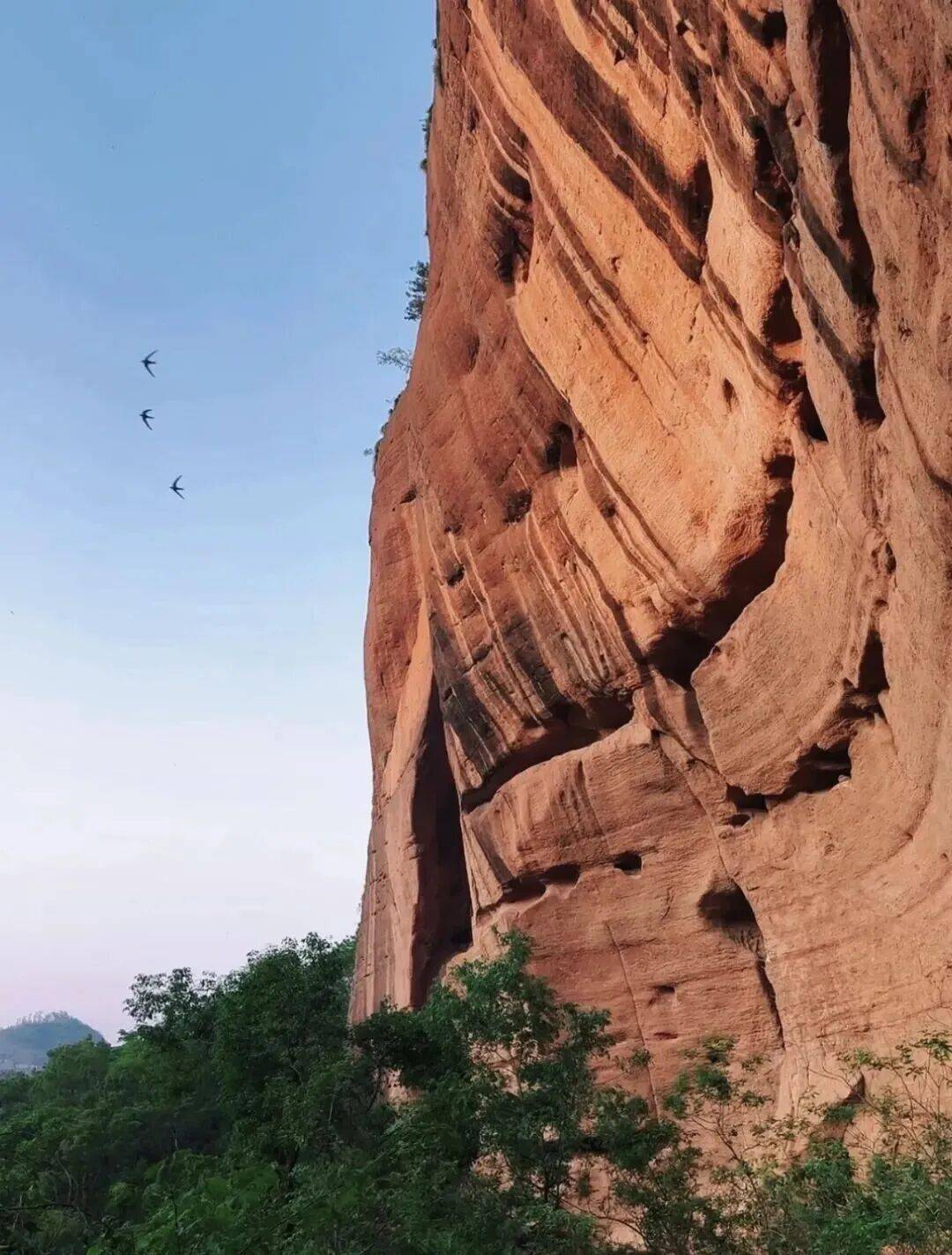 赭红色的丹霞岩壁层层叠叠风蚀出蜂窝状的孔洞在阳光照射下如火焰般